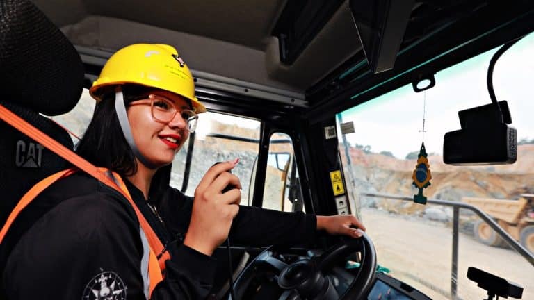 Female equipment operator wearing a yellow hard hat communicating on a radio inside a heavy machinery cab at the G Mining Ventures Tocantinzinho site.