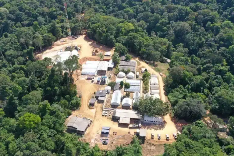 High-angle aerial view of the G Mining Ventures field camp and operations infrastructure nestled in dense rainforest.
