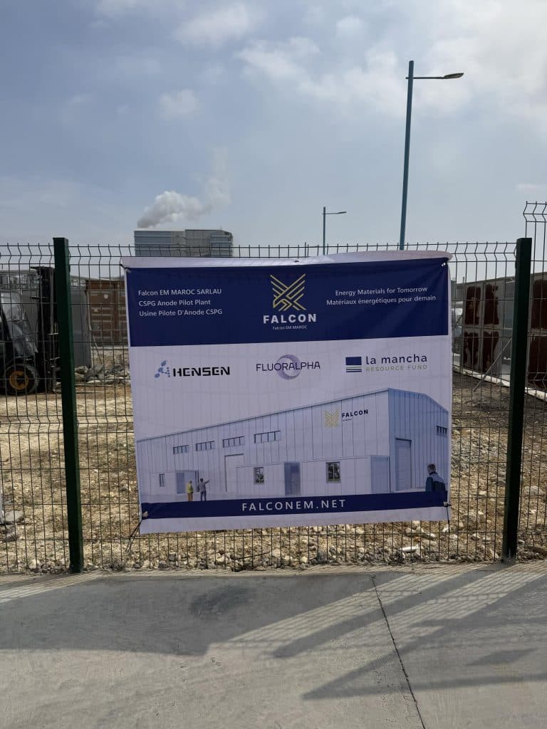 Project banner displayed on a site perimeter fence featuring the Falcon Energy Materials logo, partner logos, and architectural render for the Morocco CSPG facility development.