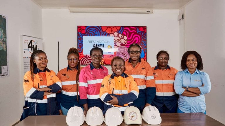 Group portrait of female employees and professionals at an Endeavour Mining office with safety hard hats lined up on the table in West Africa.