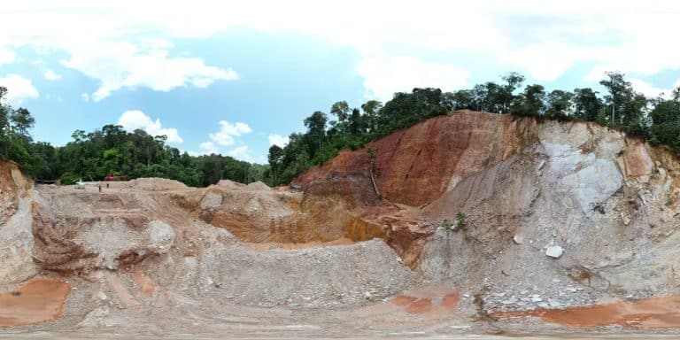 Panoramic view of a gold exploration site with exposed rock faces and surrounding rainforest.