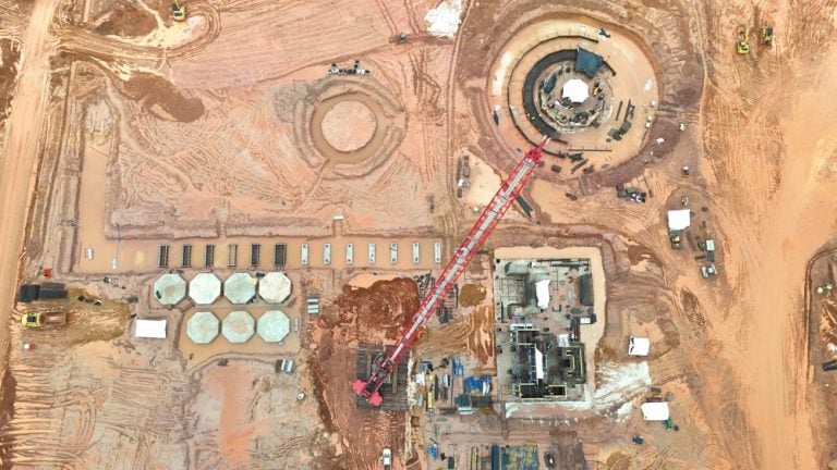Top-down aerial view of heavy construction at an Endeavour Mining gold processing plant project featuring a large red crane and circular storage tanks.
